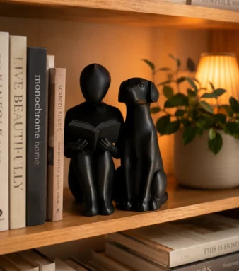 Black abstract reading and dog statue on bookshelf with books and warm lamp glow